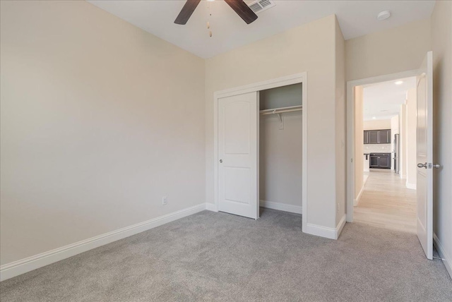 unfurnished bedroom featuring light carpet, stainless steel fridge, a closet, and ceiling fan