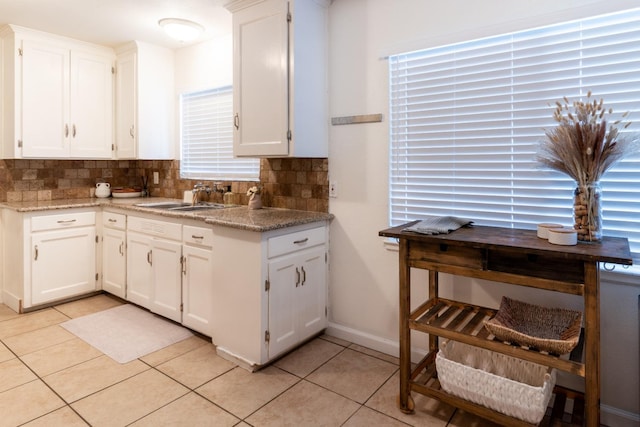 kitchen featuring decorative backsplash, light stone countertops, sink, light tile patterned floors, and white cabinets