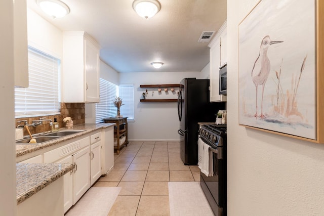 kitchen with light stone counters, sink, light tile patterned floors, black gas stove, and white cabinetry