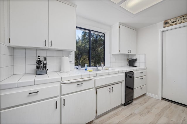 kitchen featuring white cabinets, tile countertops, a sink, light wood-type flooring, and backsplash