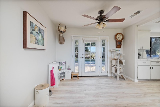 doorway to outside with light wood-type flooring, visible vents, ceiling fan, and baseboards