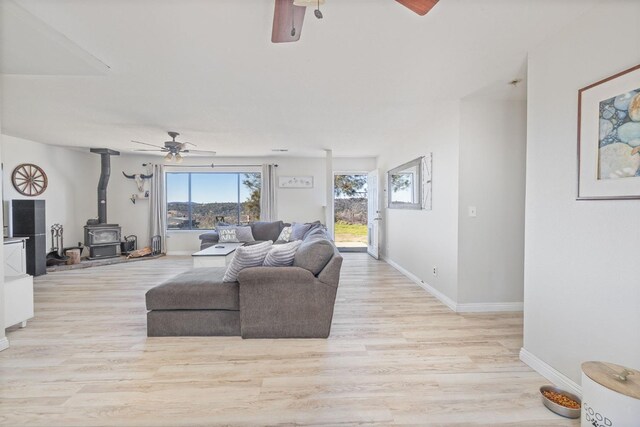 living area with light wood-style flooring, a ceiling fan, a wood stove, and baseboards