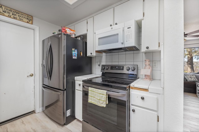 kitchen with tasteful backsplash, white cabinets, tile countertops, light wood-style flooring, and stainless steel appliances