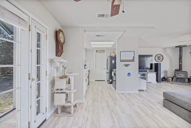 foyer featuring a wood stove, light wood finished floors, ceiling fan, and visible vents