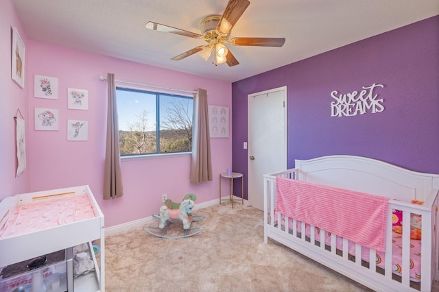 carpeted bedroom with a nursery area, a ceiling fan, and baseboards