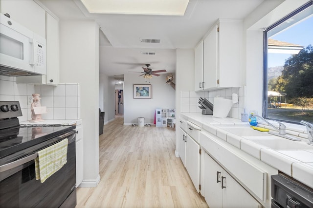 kitchen with visible vents, electric range, white microwave, light wood-style floors, and white cabinetry