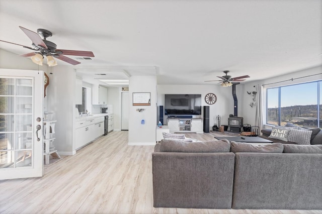 living area with a wood stove, light wood finished floors, visible vents, and a ceiling fan