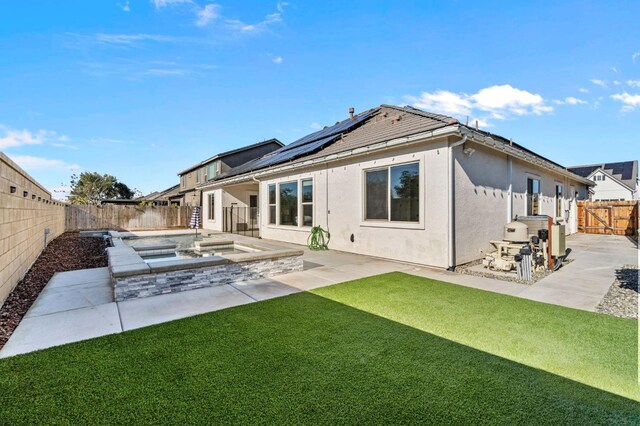 back of property with an outdoor hot tub, solar panels, a patio, and a lawn