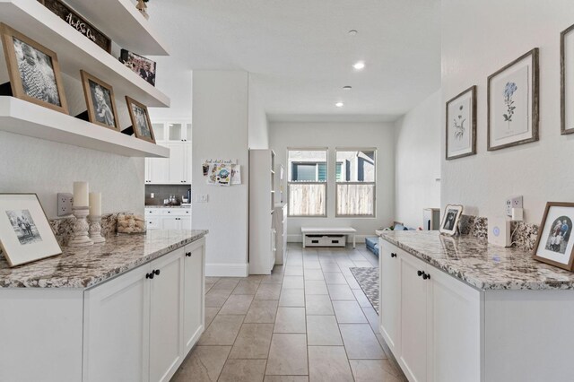 kitchen with light stone countertops, light tile patterned floors, white cabinets, fridge, and backsplash