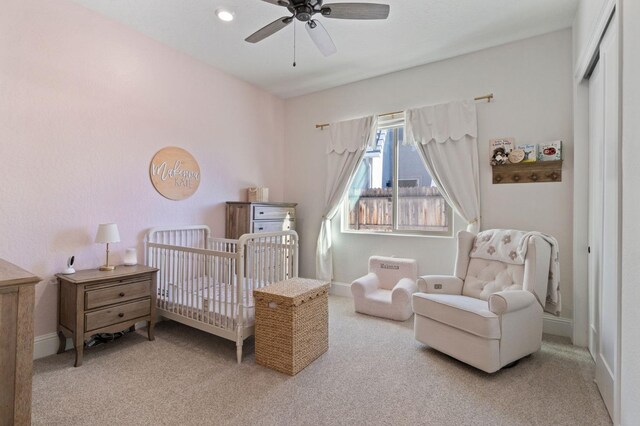 carpeted bedroom with a crib and ceiling fan