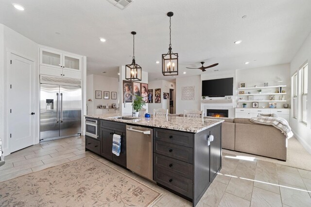 kitchen featuring built in appliances, white cabinets, ceiling fan, light stone countertops, and pendant lighting