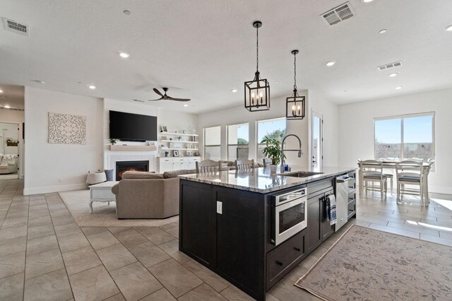 kitchen featuring light stone counters, decorative light fixtures, an island with sink, ceiling fan, and sink