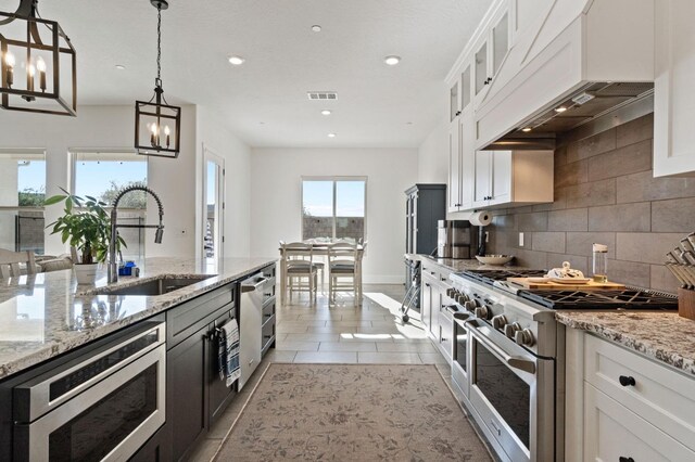 kitchen with custom exhaust hood, stainless steel appliances, sink, white cabinetry, and decorative light fixtures