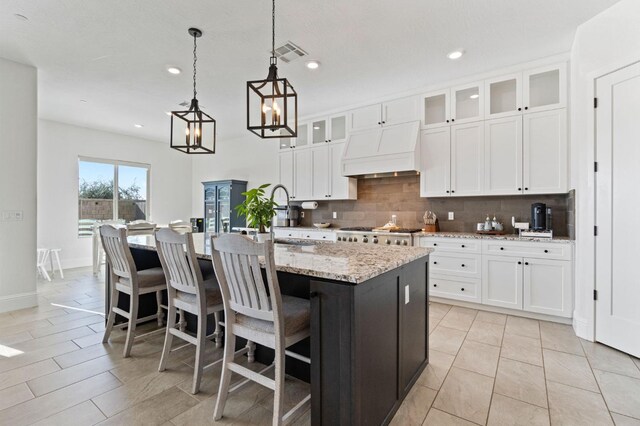 kitchen with white cabinetry, decorative light fixtures, a center island with sink, and custom range hood