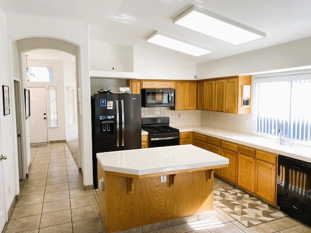 kitchen featuring a kitchen breakfast bar, tile counters, a center island, black appliances, and tasteful backsplash