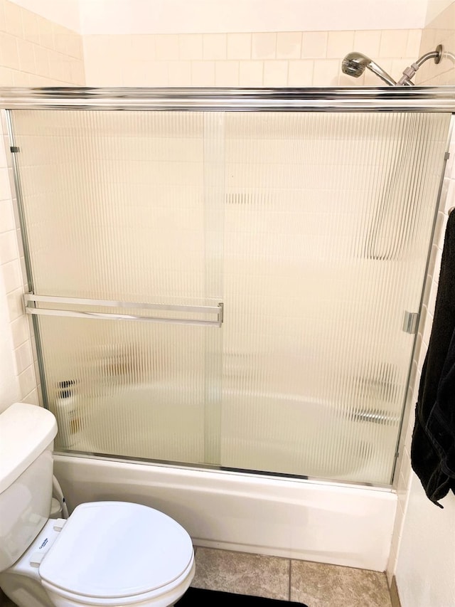 full bath featuring toilet, tile patterned flooring, and combined bath / shower with glass door