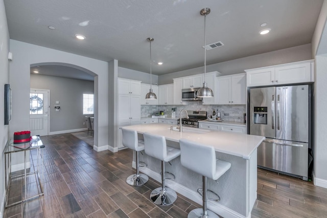 kitchen featuring stainless steel appliances, a center island with sink, pendant lighting, and white cabinetry