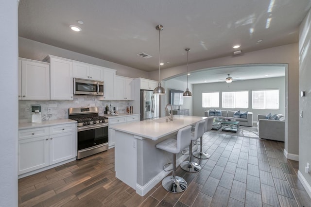 kitchen with a center island with sink, decorative light fixtures, white cabinetry, and appliances with stainless steel finishes