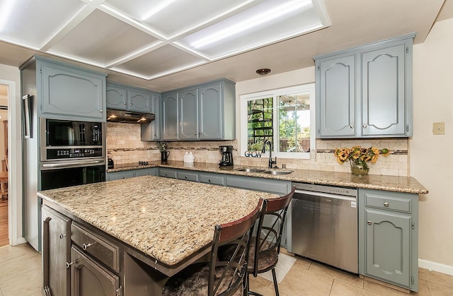 kitchen featuring sink, a center island, light stone counters, light tile patterned flooring, and appliances with stainless steel finishes