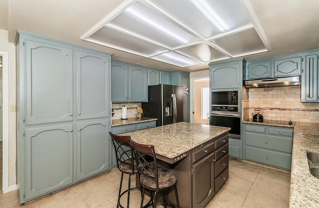 kitchen with stainless steel appliances, a center island, light stone counters, light tile patterned floors, and decorative backsplash