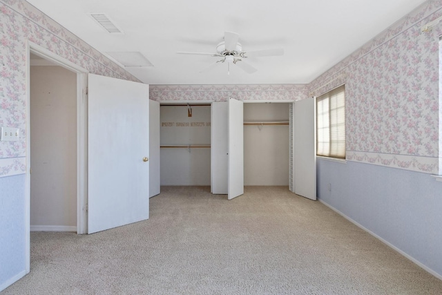 unfurnished bedroom with ceiling fan, light colored carpet, and multiple closets