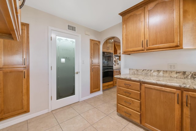 kitchen with black double oven, light stone counters, and light tile patterned floors