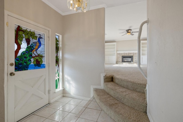 tiled entrance foyer featuring ceiling fan with notable chandelier, a brick fireplace, and ornamental molding