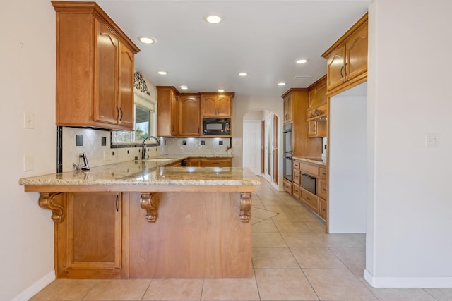 kitchen with kitchen peninsula, black appliances, backsplash, a kitchen breakfast bar, and sink