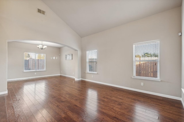 empty room featuring dark hardwood / wood-style flooring, high vaulted ceiling, a wealth of natural light, and a chandelier