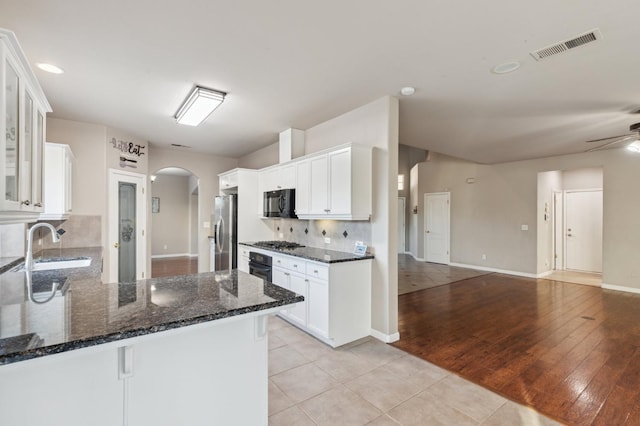 kitchen featuring kitchen peninsula, light tile patterned floors, black appliances, white cabinets, and dark stone counters