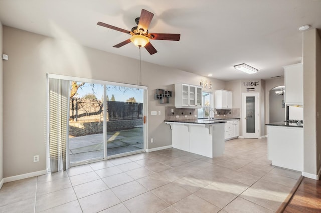 kitchen featuring white cabinets, light tile patterned flooring, ceiling fan, kitchen peninsula, and decorative backsplash