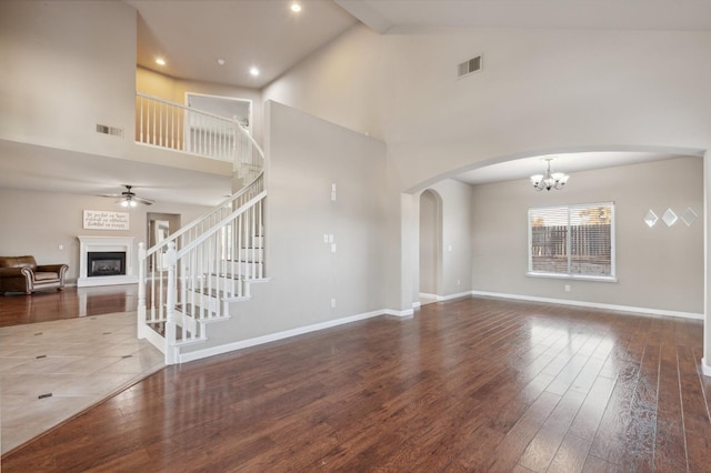 unfurnished living room with ceiling fan with notable chandelier, high vaulted ceiling, and hardwood / wood-style floors