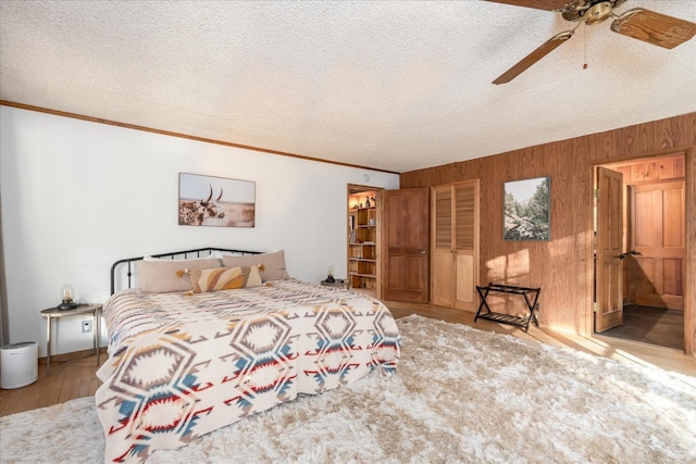 bedroom featuring wooden walls, a textured ceiling, ceiling fan, and ornamental molding