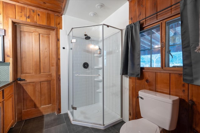 bathroom featuring toilet, tile patterned flooring, a shower with door, and wood walls