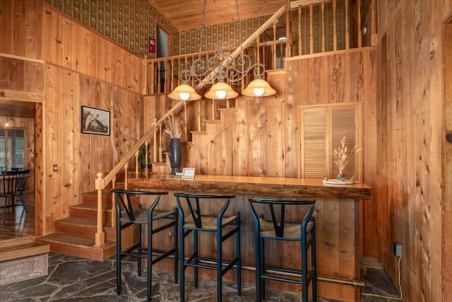 bar featuring a towering ceiling, wooden walls, decorative light fixtures, and wood ceiling