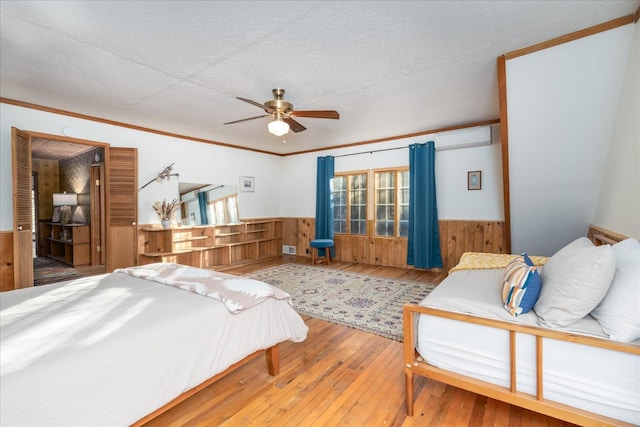 bedroom with a textured ceiling, a wall unit AC, ceiling fan, and wood-type flooring