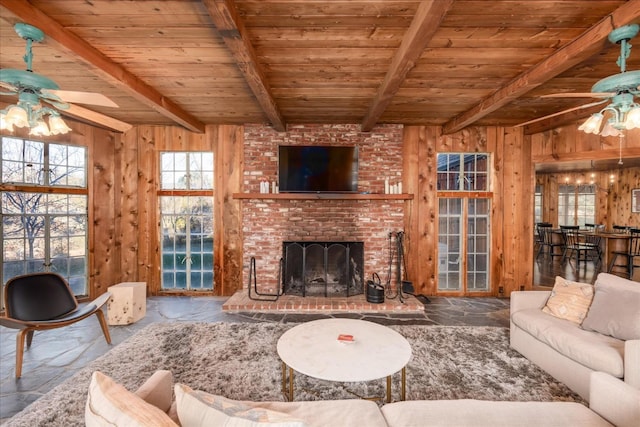 living room featuring a brick fireplace, wood walls, ceiling fan, and beam ceiling