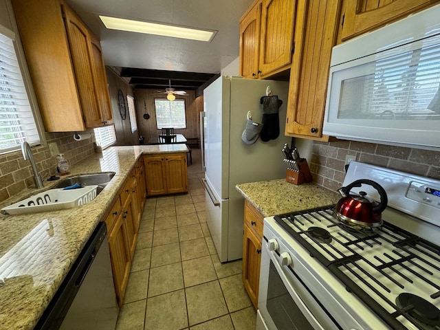 kitchen with white appliances, light stone counters, light tile patterned floors, backsplash, and sink