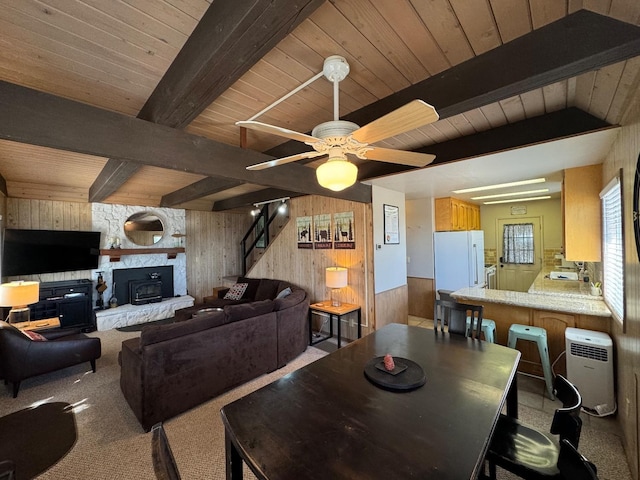 carpeted dining room with ceiling fan, beam ceiling, and wooden walls