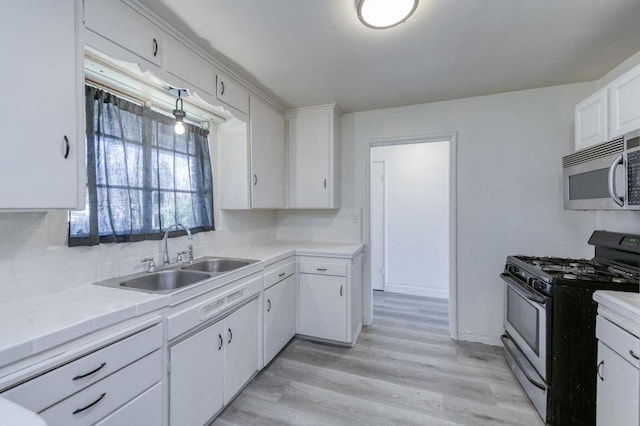 kitchen featuring tile counters, light hardwood / wood-style floors, gas range oven, sink, and white cabinetry