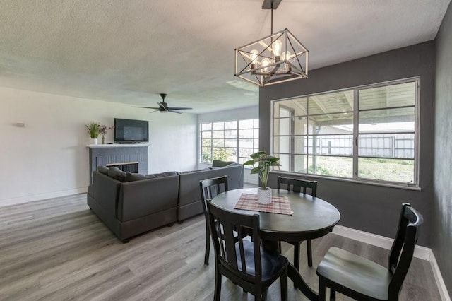 dining space featuring ceiling fan with notable chandelier, a fireplace, and hardwood / wood-style floors