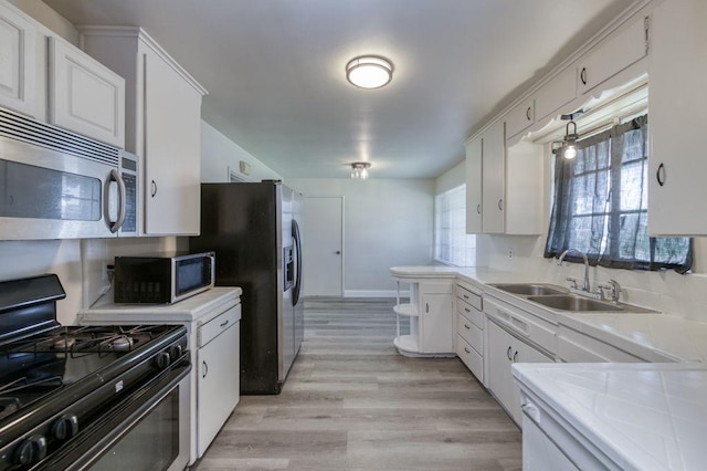 kitchen featuring decorative light fixtures, light hardwood / wood-style floors, black gas stove, white cabinetry, and sink