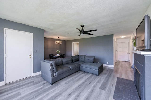 living room with light hardwood / wood-style floors, ceiling fan with notable chandelier, and a textured ceiling