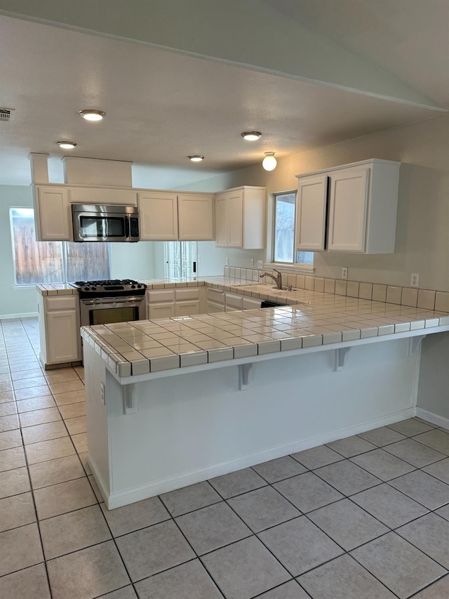 kitchen with stainless steel appliances, white cabinetry, tile countertops, and kitchen peninsula