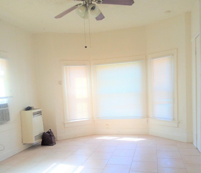 tiled spare room featuring heating unit, ceiling fan, and a healthy amount of sunlight