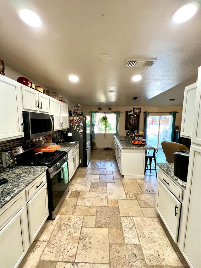 kitchen with stainless steel appliances, light stone countertops, white cabinets, and plenty of natural light