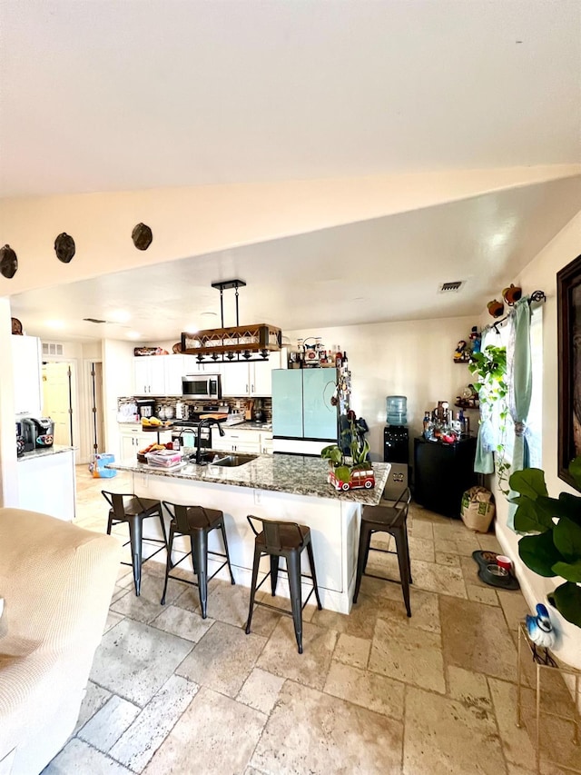 kitchen with vaulted ceiling, refrigerator, a breakfast bar, white cabinets, and dark stone counters