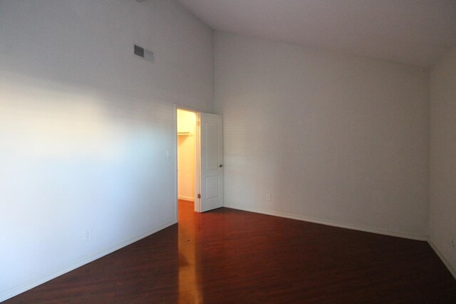 empty room featuring high vaulted ceiling and dark wood-type flooring