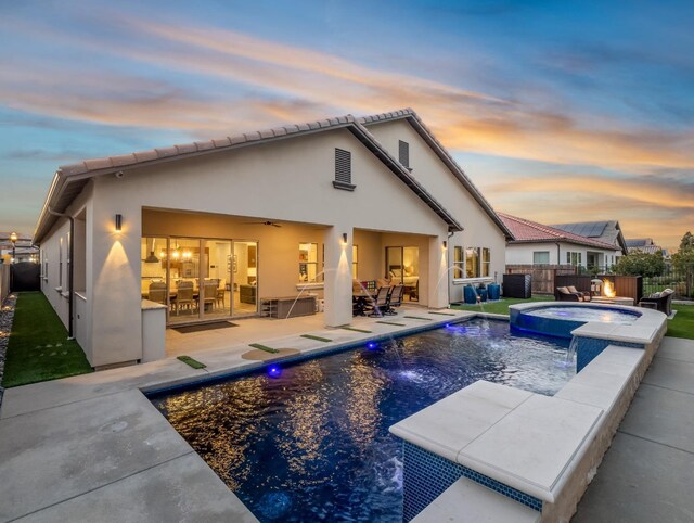 back house at dusk with a pool with hot tub, pool water feature, a patio area, and ceiling fan