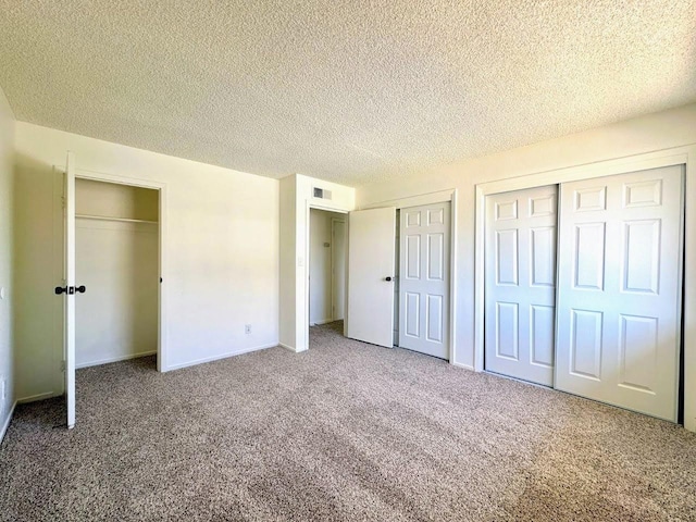 unfurnished bedroom with carpet floors, a textured ceiling, and two closets